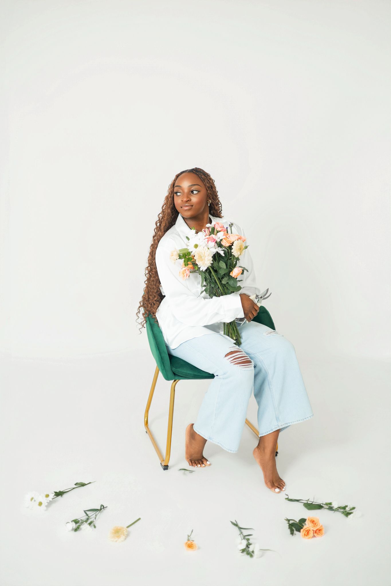 Artistic portrait with scattered flowers and soft lighting against white backdrop.