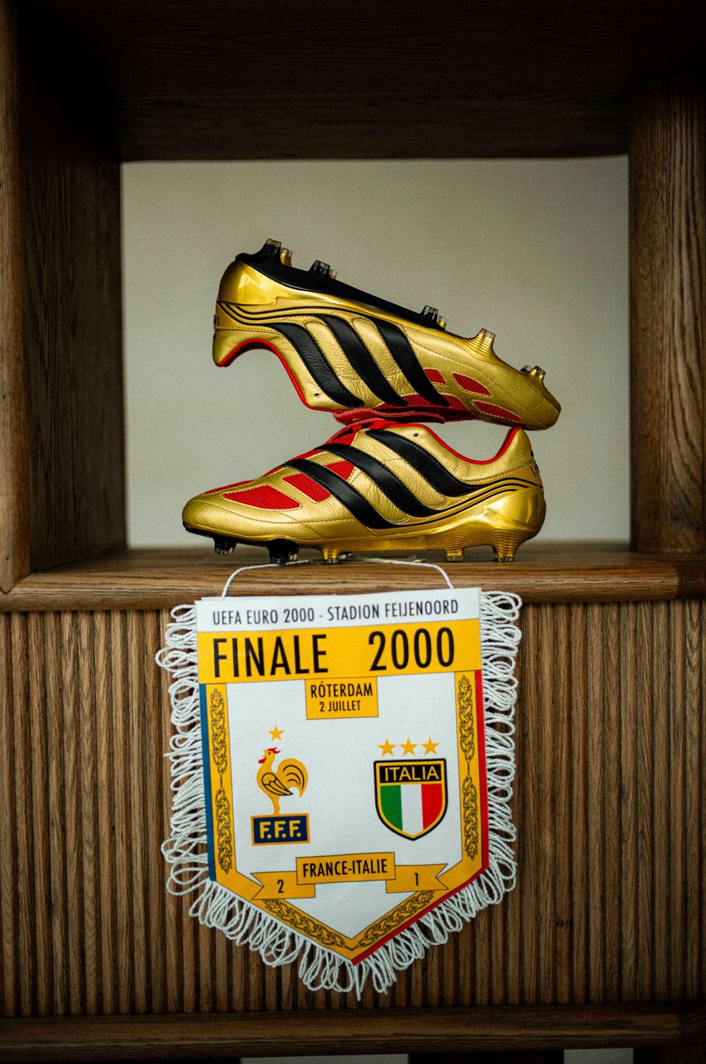 Gold and black Adidas soccer cleats displayed on wooden shelves alongside championship pennants and memorabilia.