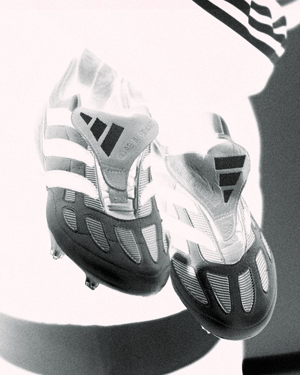 Black and white artistic photo of classic Adidas soccer cleats casting dramatic shadows.