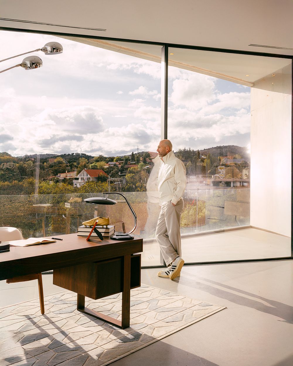 A person in protective white coveralls inspects a modern interior space with large windows overlooking a scenic landscape.