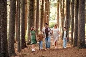 Family of four walking through tall pine forest on a sunny day, wearing casual clothes on a pine needle covered path.