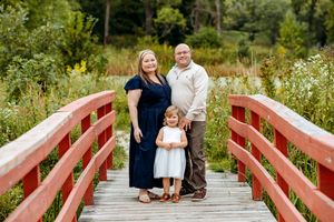 A couple shares a tender moment on a red wooden bridge surrounded by lush summer greenery and wildflowers.