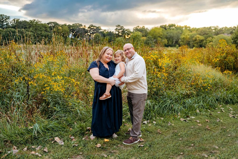 A couple embraces in a golden meadow filled with wildflowers during sunset on a warm autumn evening.