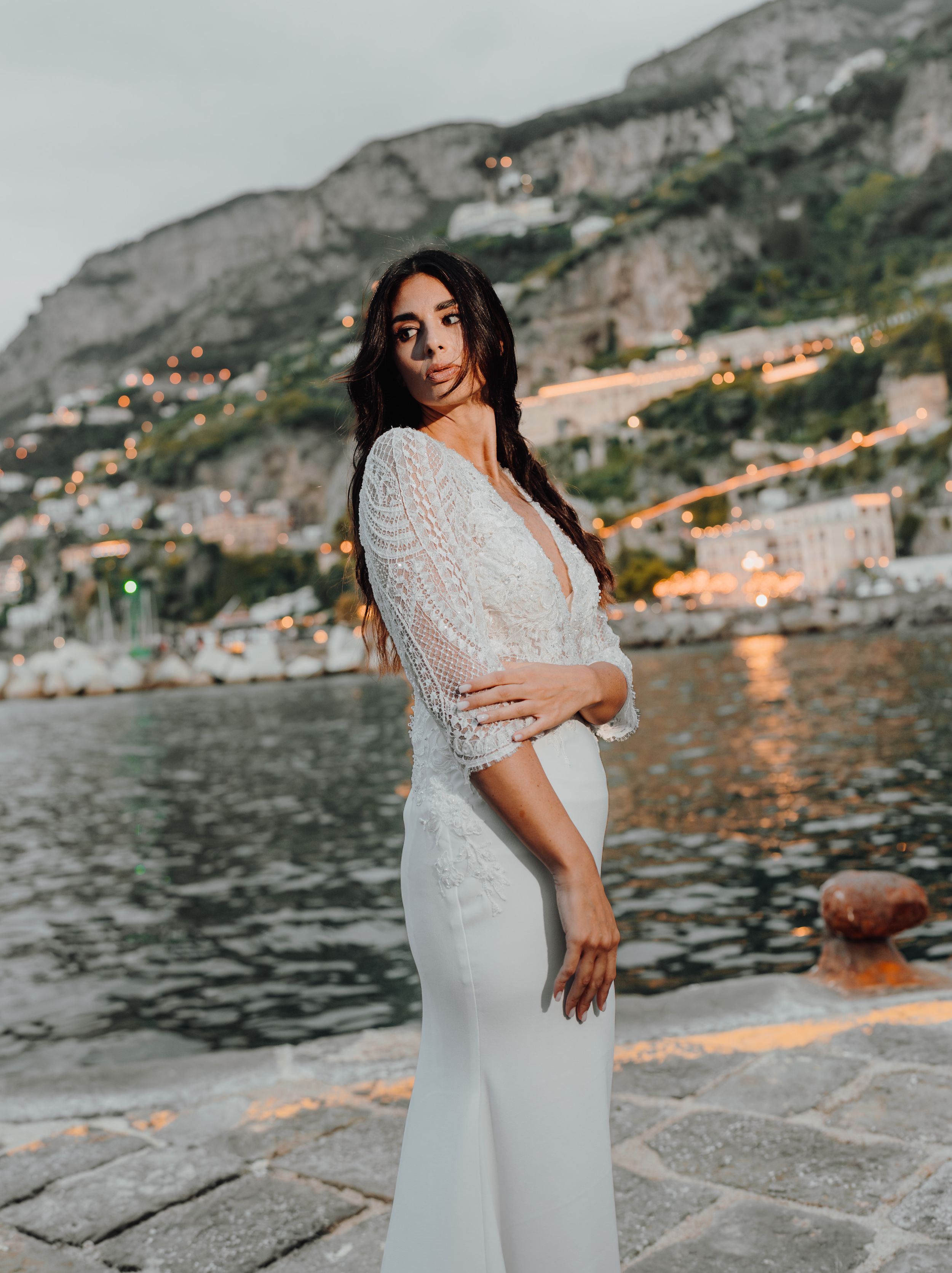 A stunning sunset photoshoot along the Amalfi Coast waterfront with a white lace gown against the golden coastal backdrop.