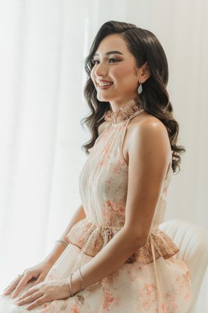 A person in a floral halter neck dress with vintage-style waves smiles while sitting against a white background.