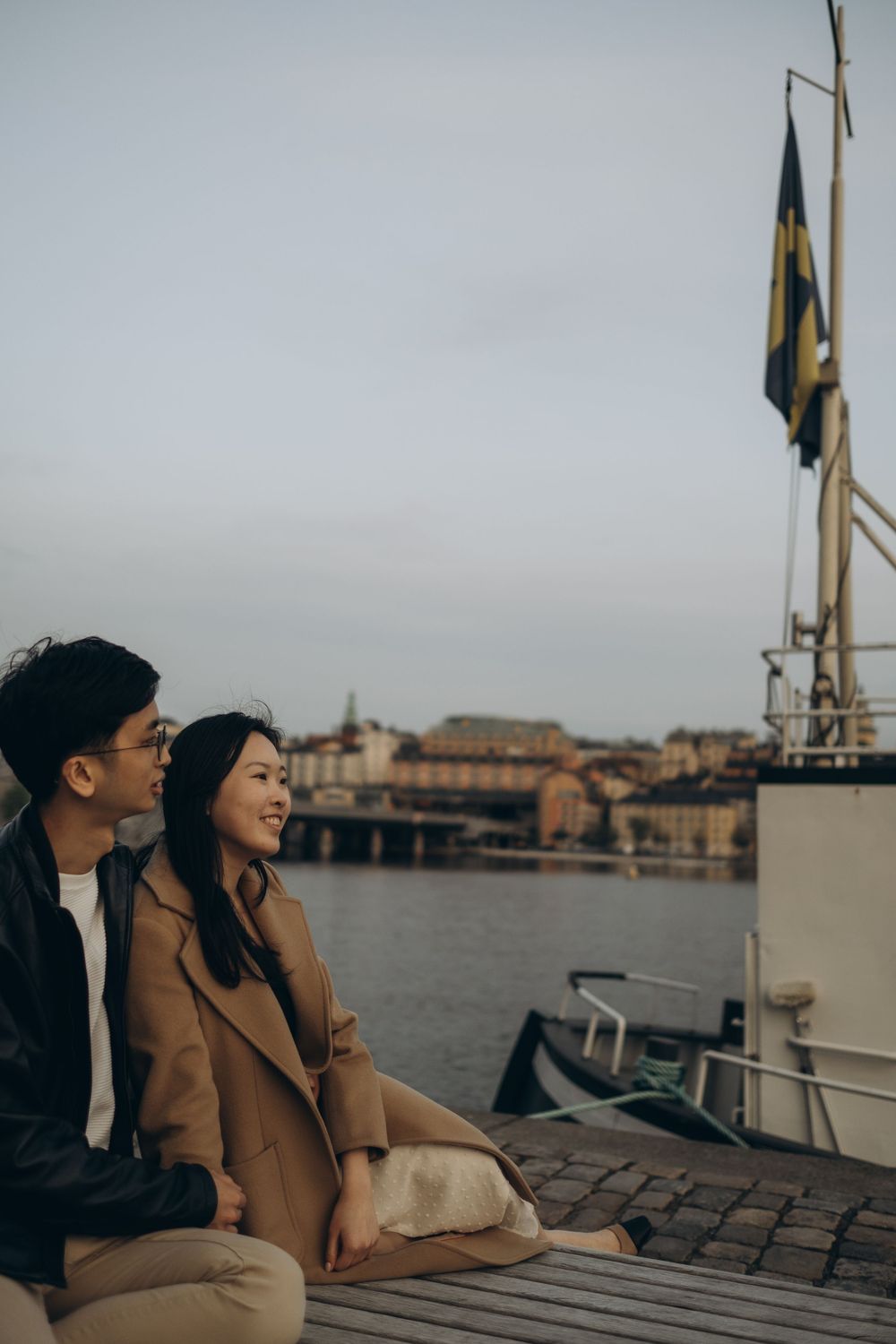couple sitting in a harbor at Riddarholmen looking at view during vacation photoshoot in Stockholm