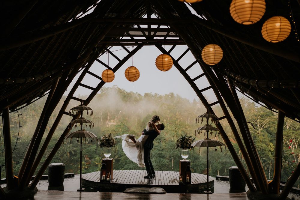 Rustic wedding venue with orange paper lanterns hanging from wooden beams against forest backdrop.