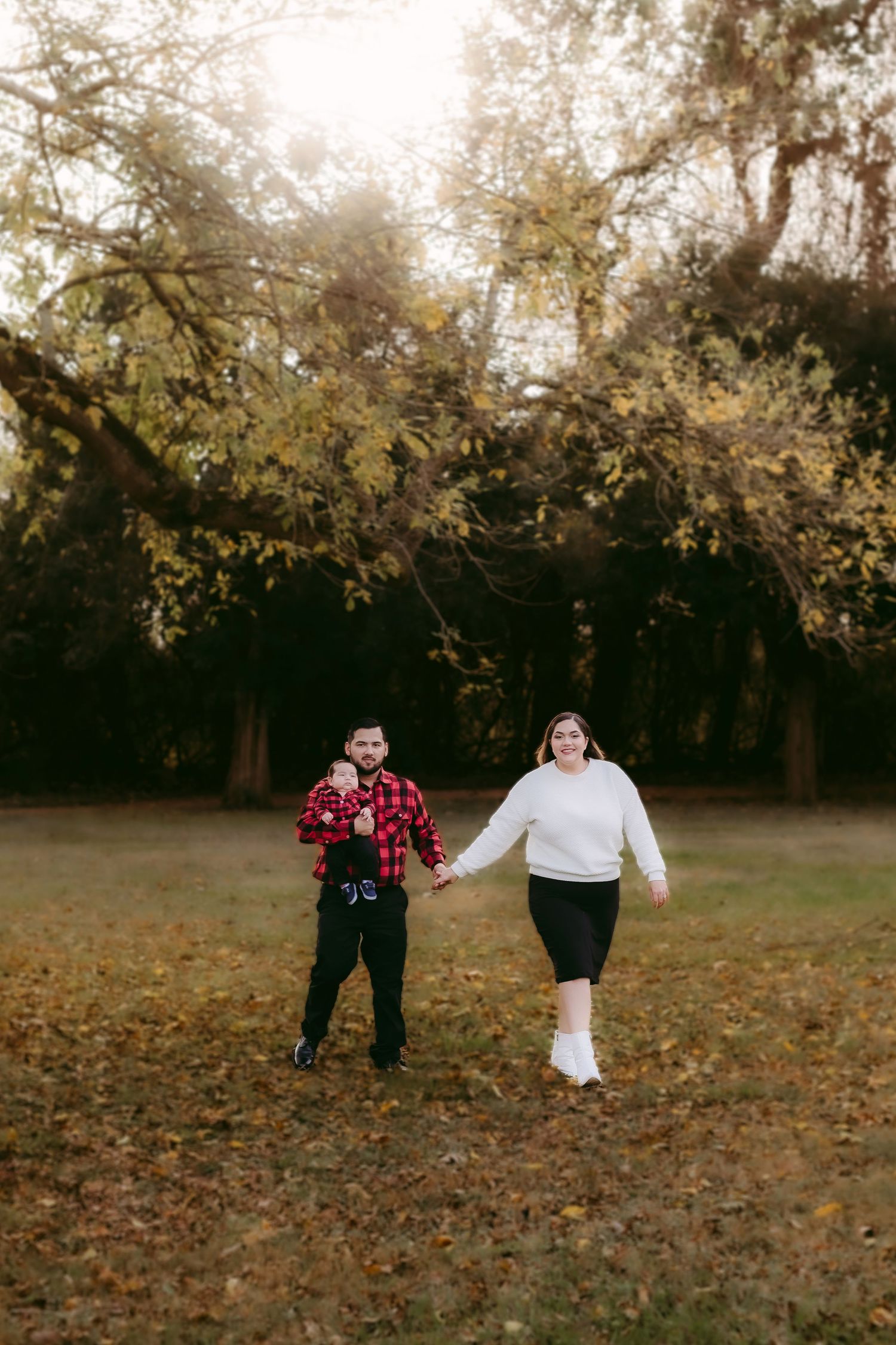 A couple walks hand in hand through a fall field with golden autumn leaves scattered on the ground. Victoria, Texas