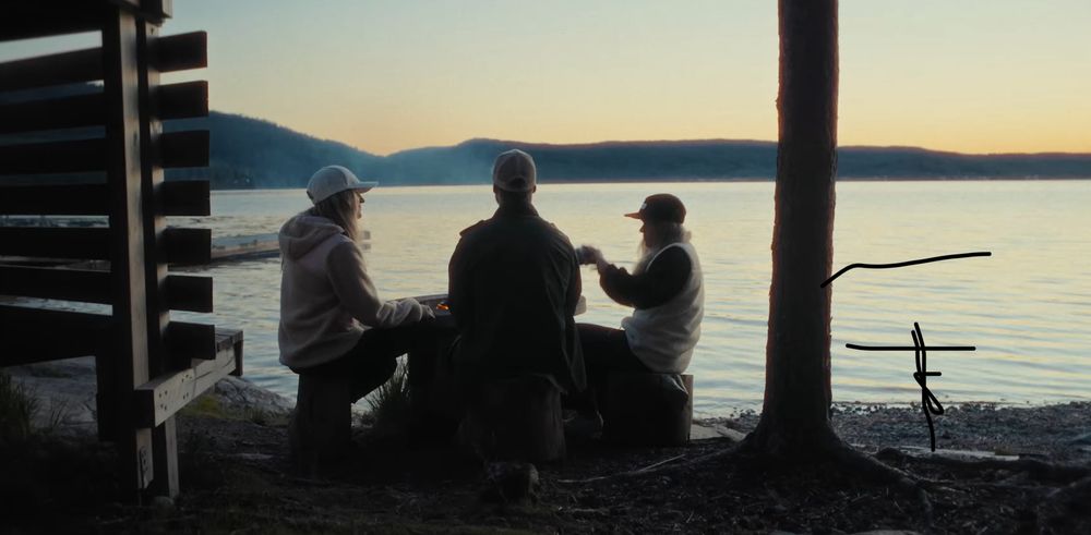 Silhouettes of people sitting on a wooden dock watching the sunset over a tranquil lake.