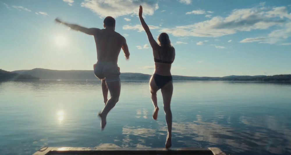 Silhouettes of people jumping joyfully against a sunset sky reflected in calm water.