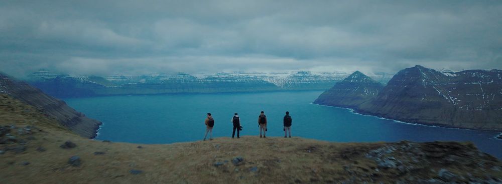 Group of hikers overlooking a turquoise fjord surrounded by mountain peaks.