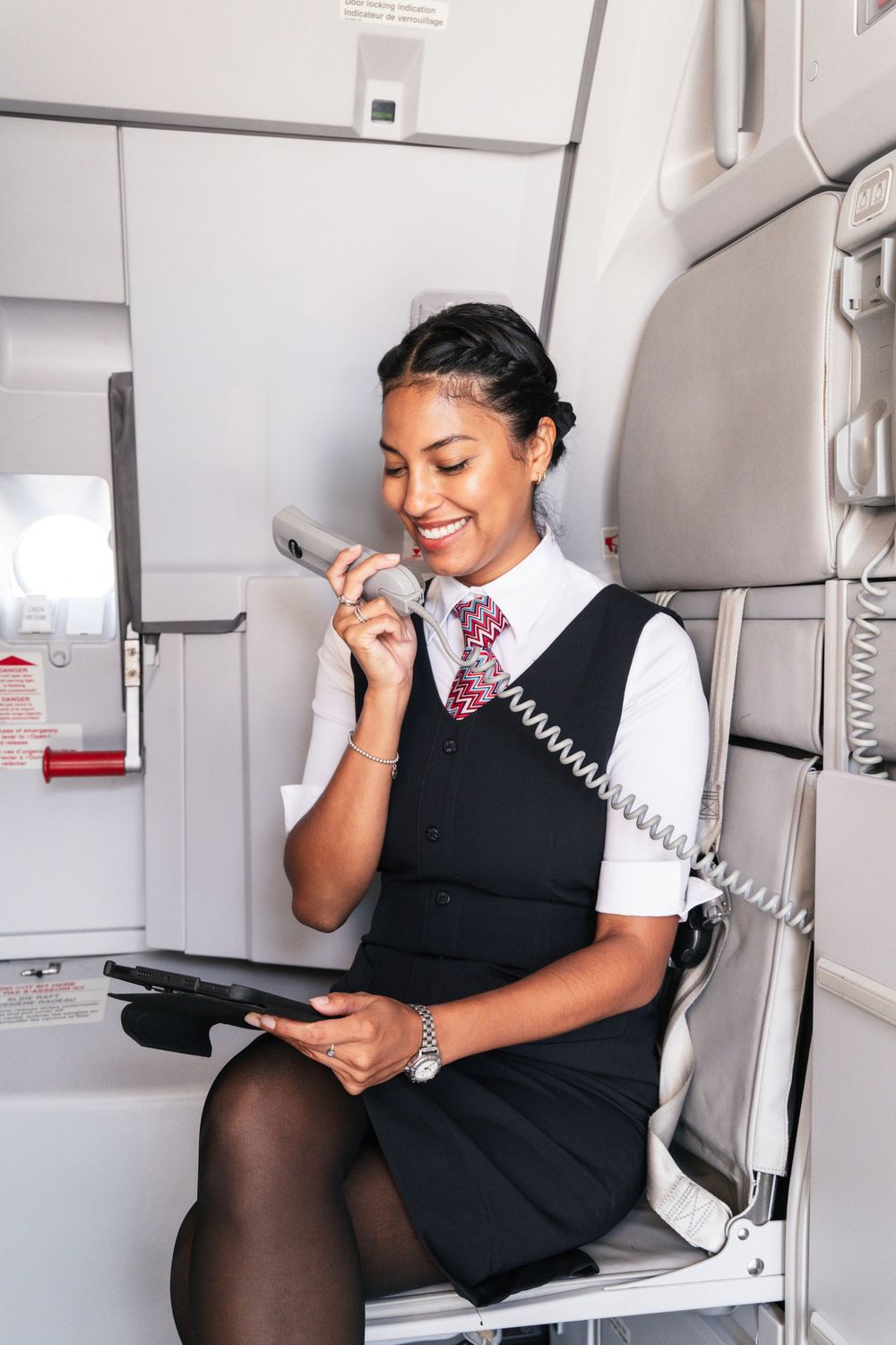Flight attendant in uniform smiles while making an announcement on the airplane intercom system.