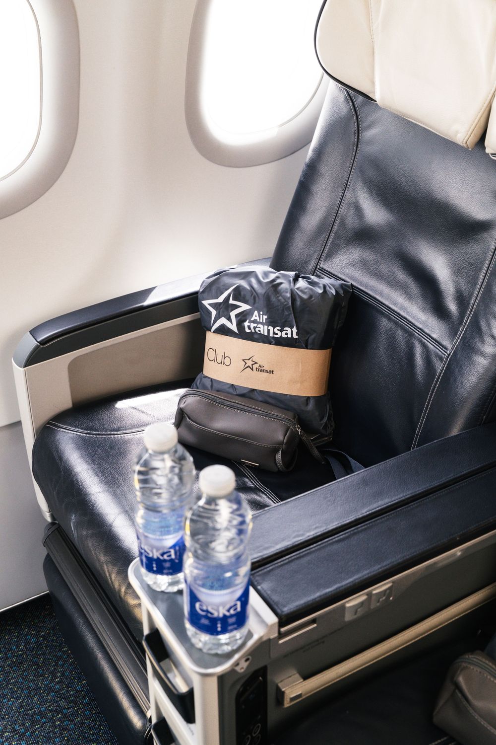 Four airline business class seats with black leather upholstery and water bottles arranged in a row near airplane windows.