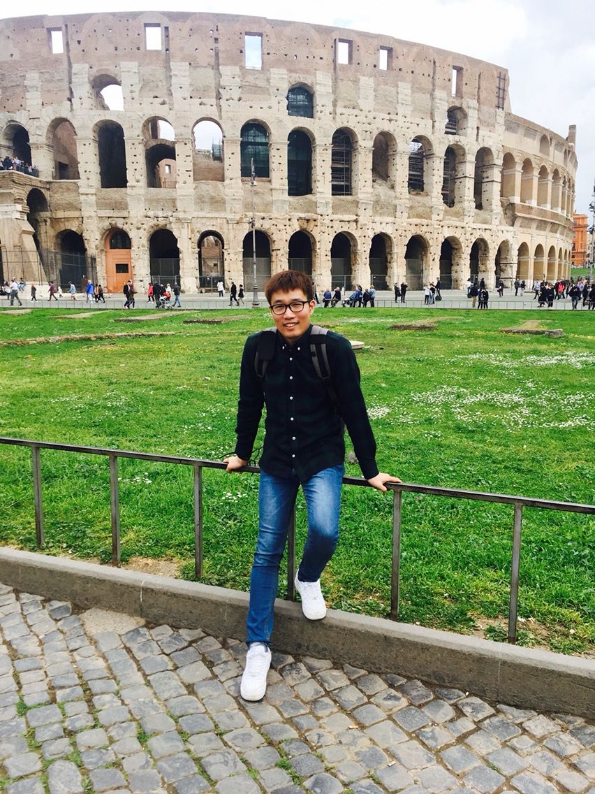 Tourist posing near the historic Colosseum in Rome with ancient stone walls and arches visible in the background.