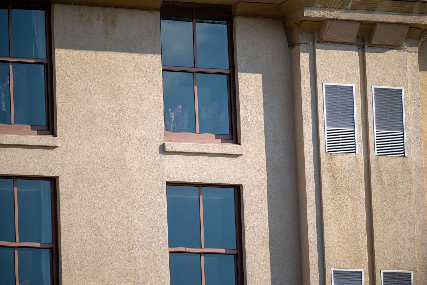 Beige stucco building exterior with dark framed windows showing architectural detail in sunlight.