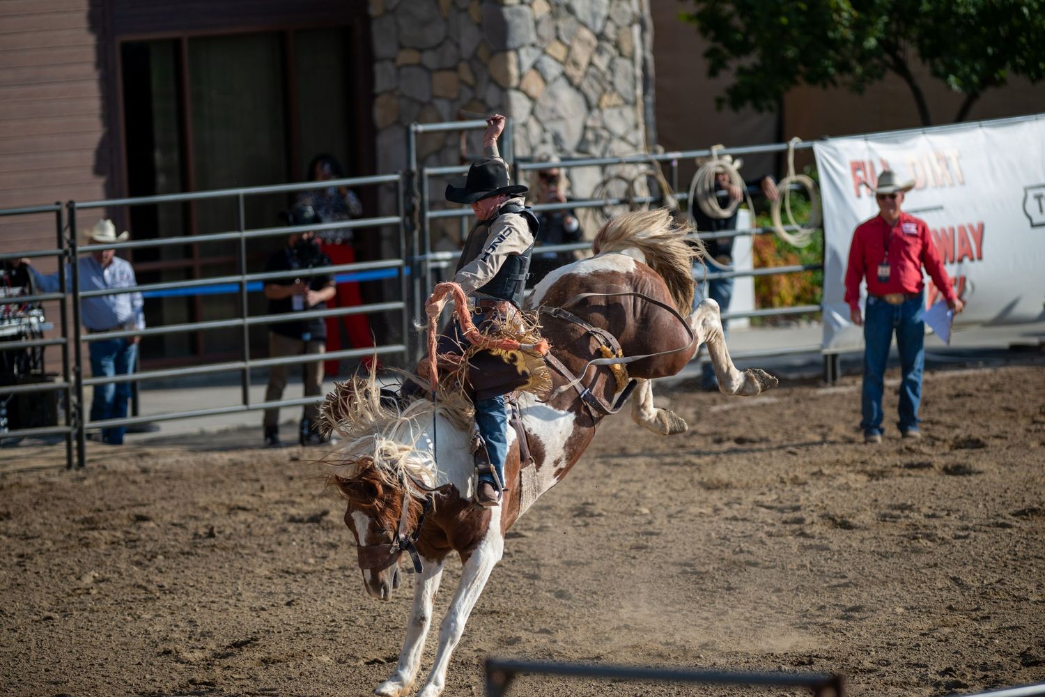 A rider falls off a bucking bronco during a rodeo competition in a dirt arena.
