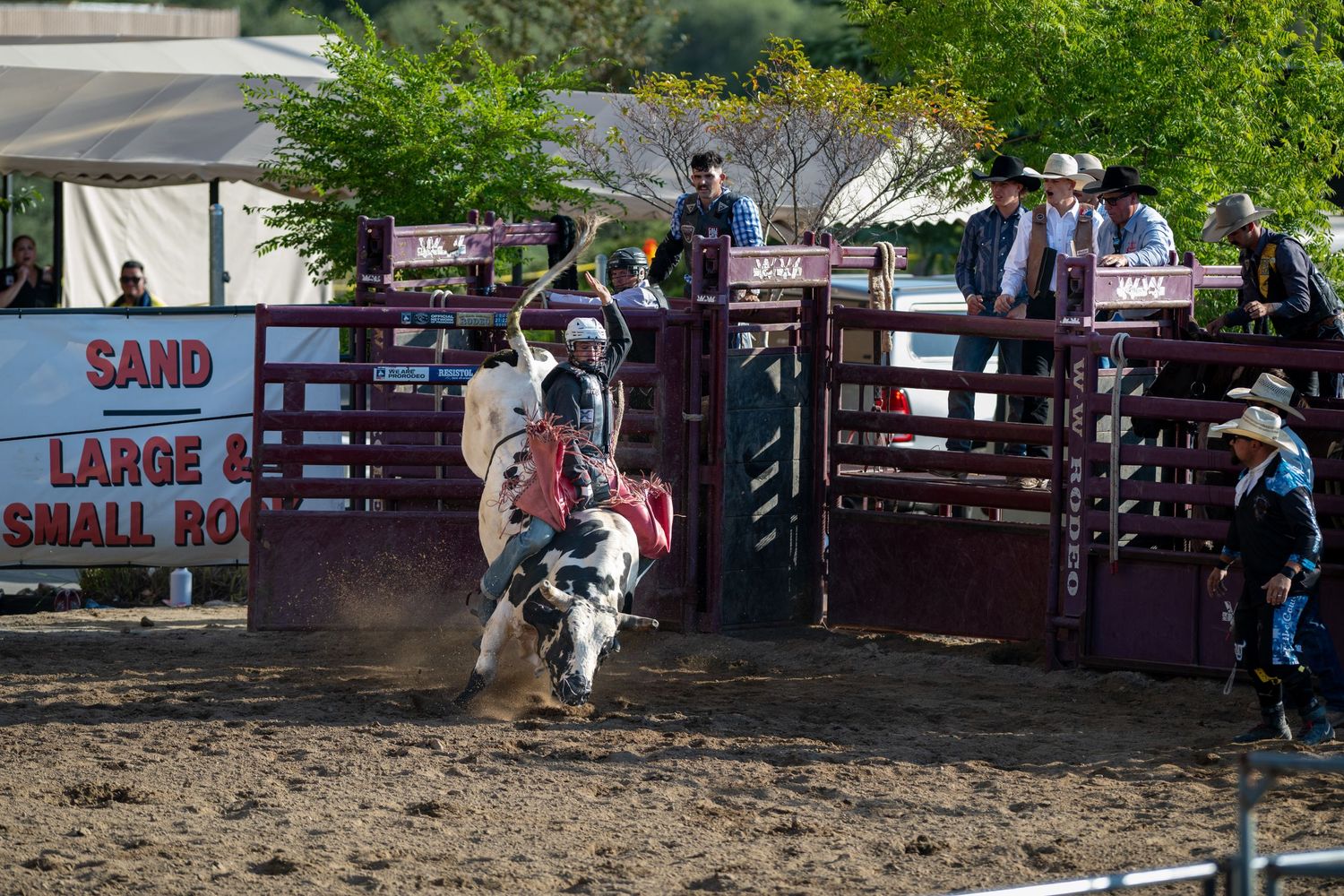 Cowboy rides on a bucking horse during an intense rodeo competition in a dirt arena with arena fences visible.