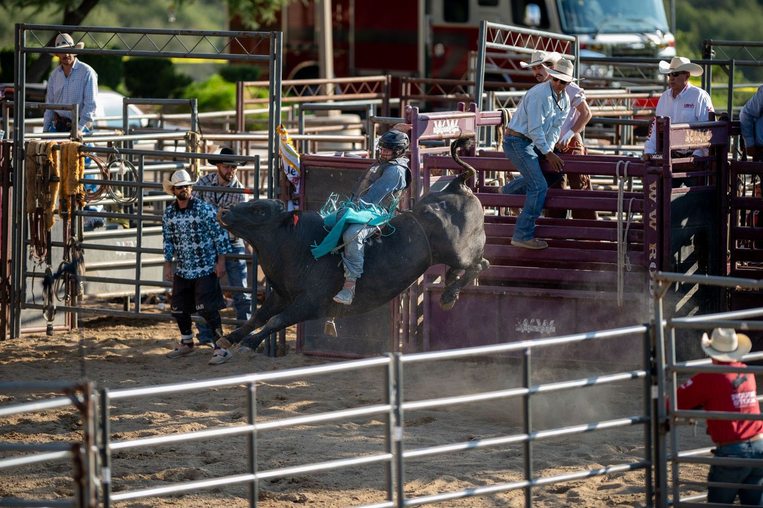 A person rides a horse around a dusty rodeo arena as spectators watch from behind the fence during a competition.