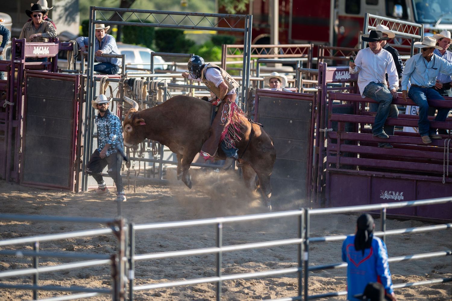 A group of people watching a cowboy attempt to ride a bucking bull at a rodeo event in an outdoor arena.