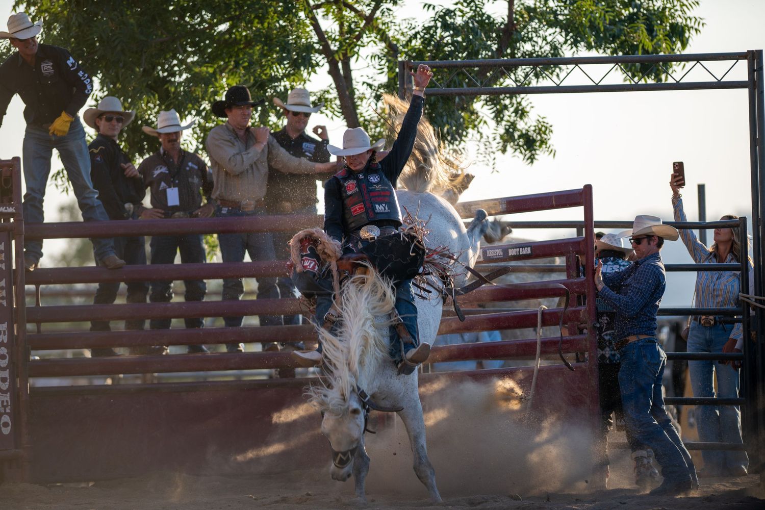 A bull rider hangs on tight during a rodeo competition as spectators watch from wooden bleachers in the background.