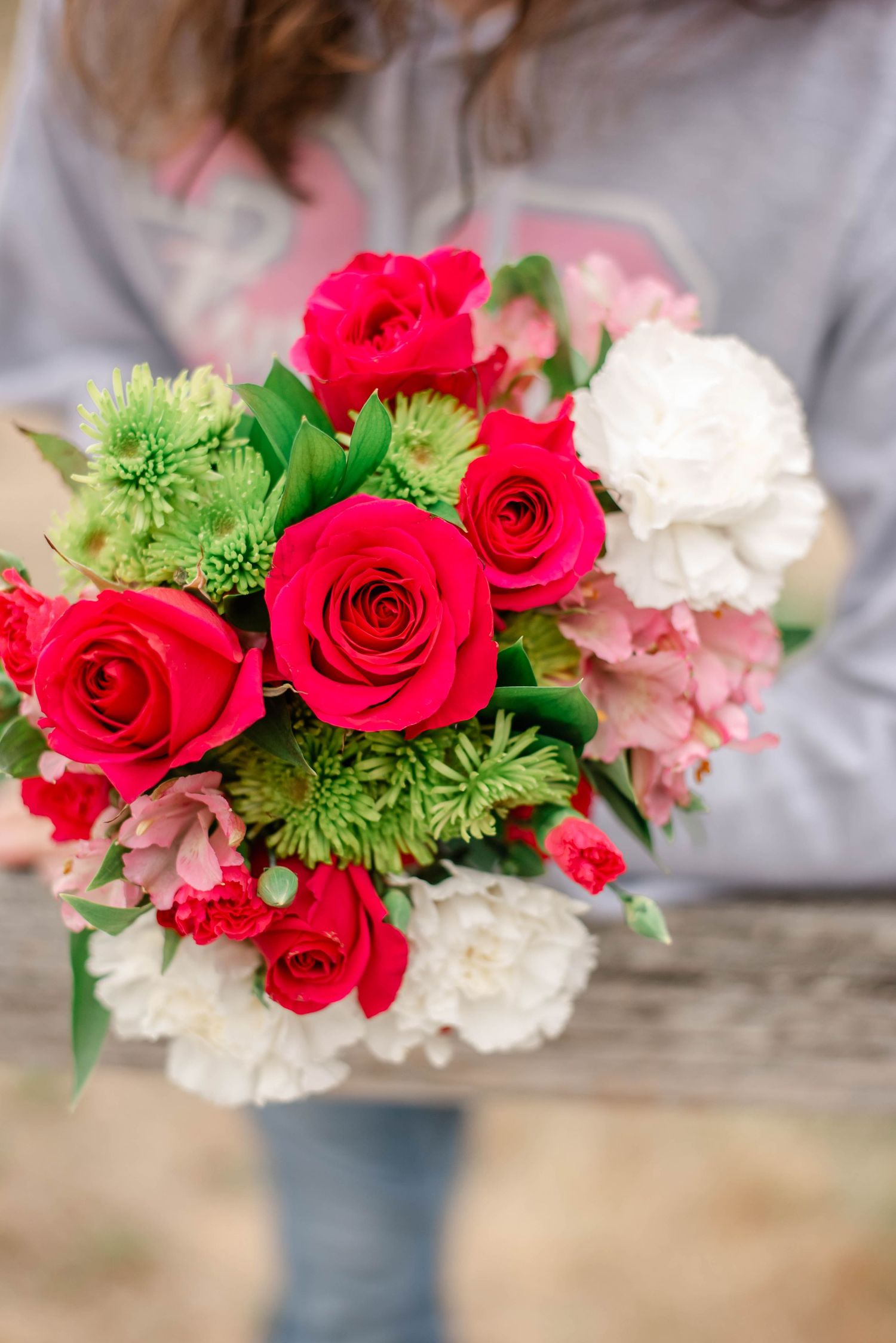 Beautiful floral arrangement featuring bright red roses, white carnations, and green chrysanthemums in a rustic setting.