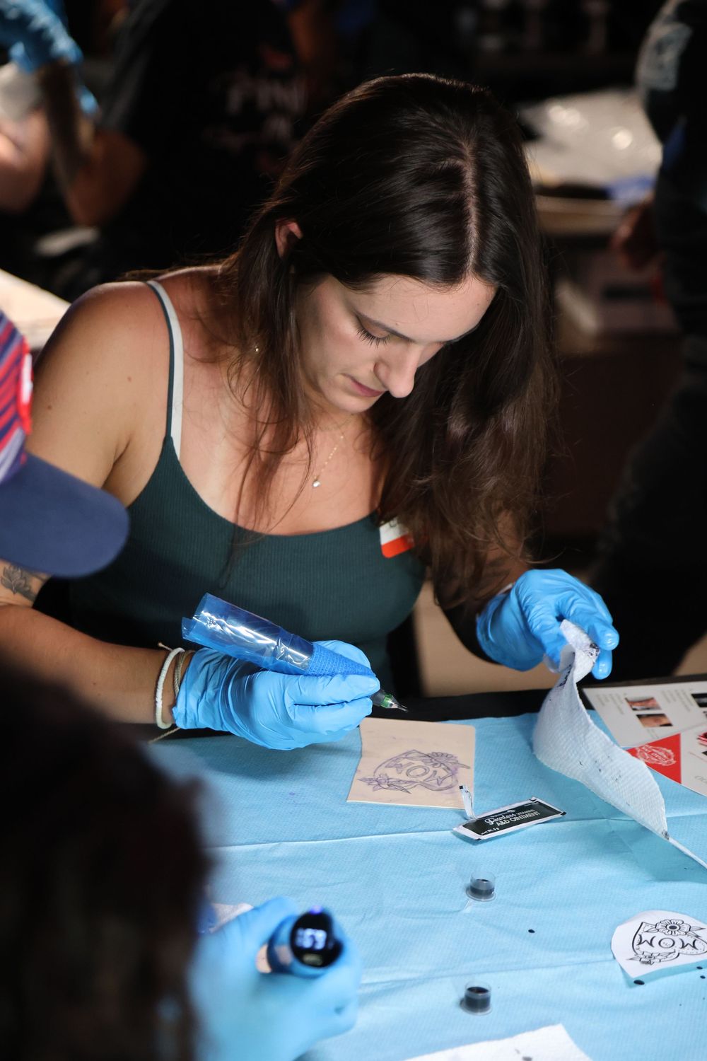 Person wearing blue gloves writes uses tattoo gun to outline tattoo on fake skin.