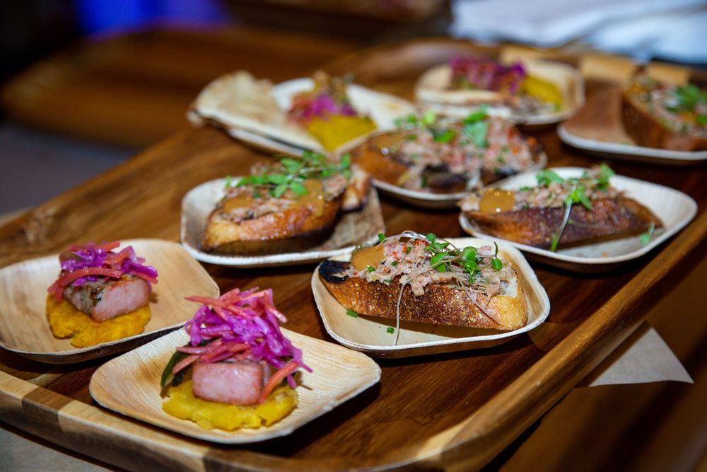 Colorful gourmet sliders with toppings and garnishes arranged on wooden plates at a restaurant setting.