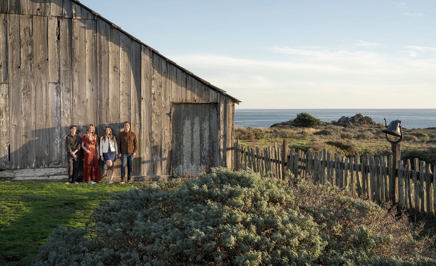 A rustic wooden barn stands on the coastline at Sea Ranch, California during golden hour.