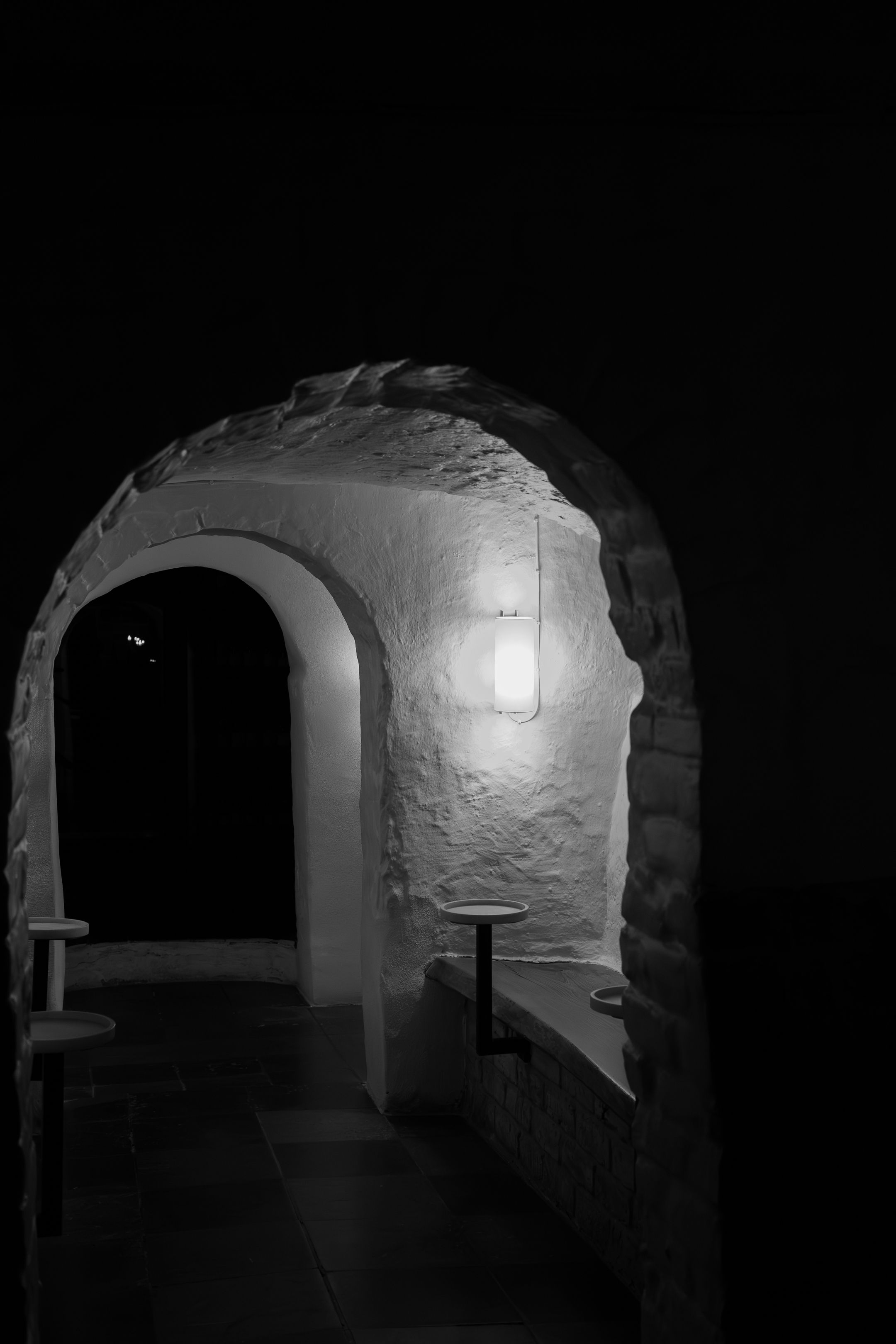 Dark stone tunnel with arched passageways and white walls illuminated by dim lighting.