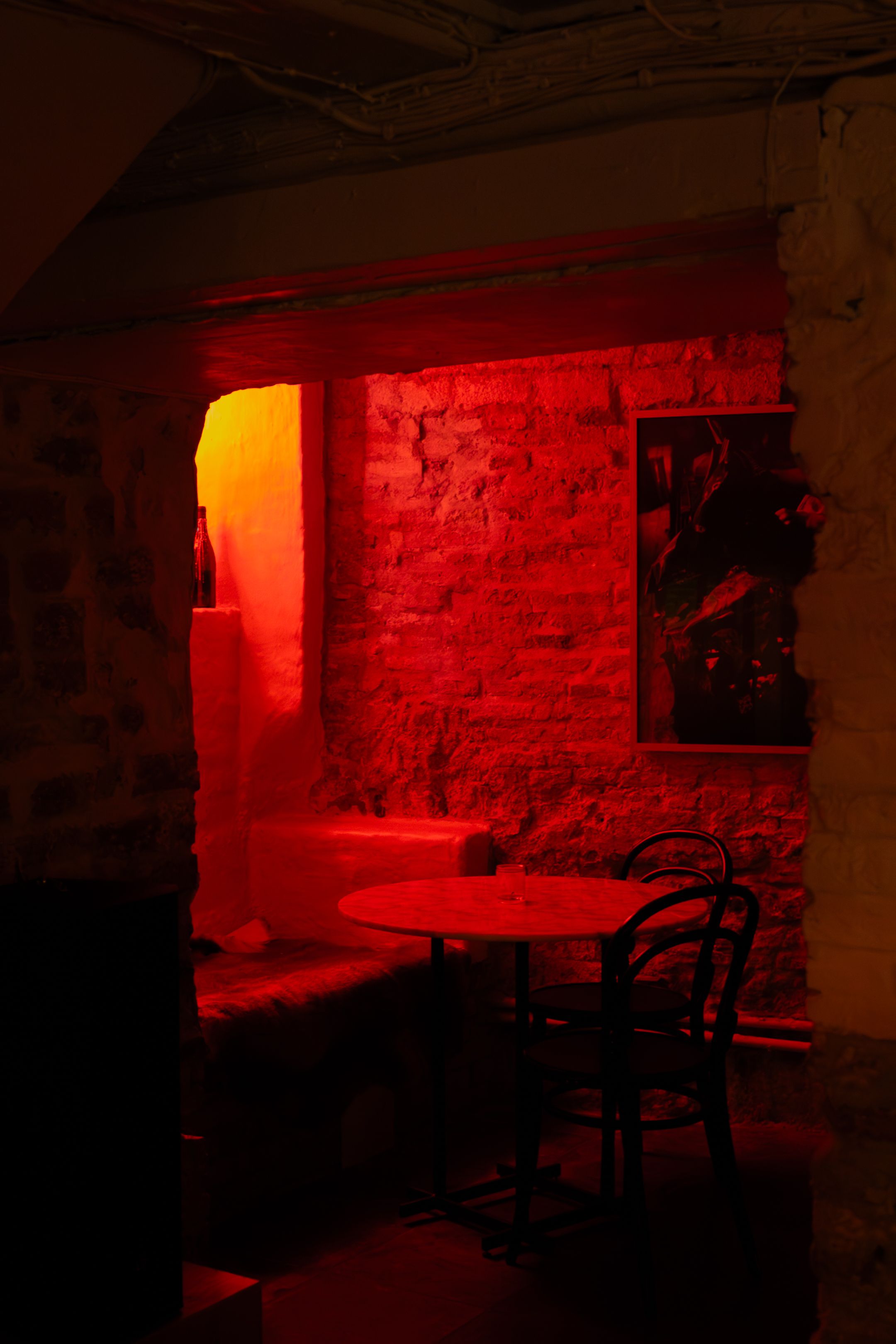 A dimly lit basement corridor illuminated by red lighting creates an eerie underground atmosphere.