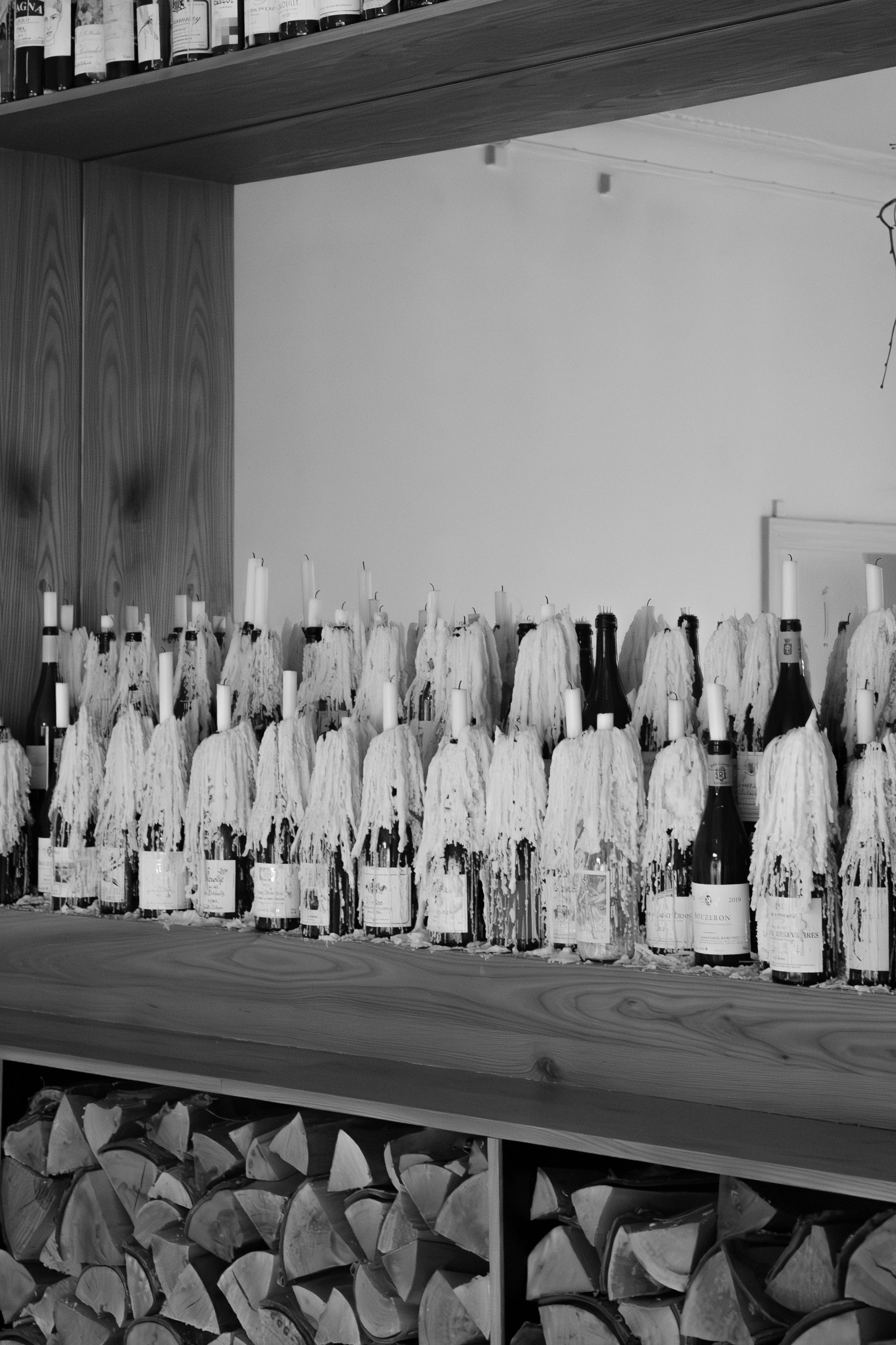 Long shelf displaying wrapped wine bottles arranged in neat rows with black and white coverings.