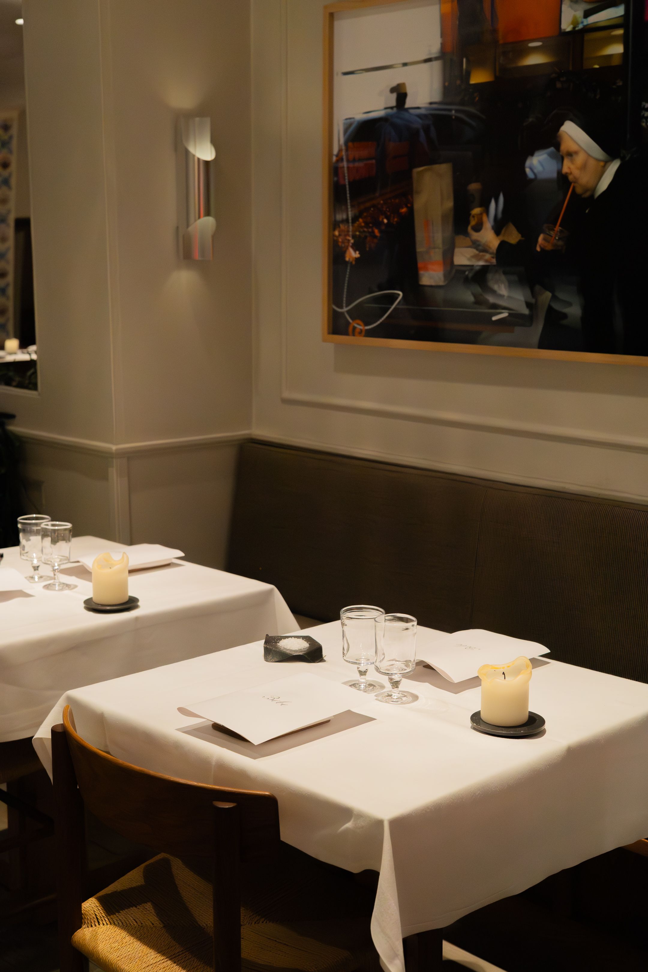 Elegant restaurant interior with white tablecloths, candles, and framed artwork on the wall creating an intimate dining atmosphere.