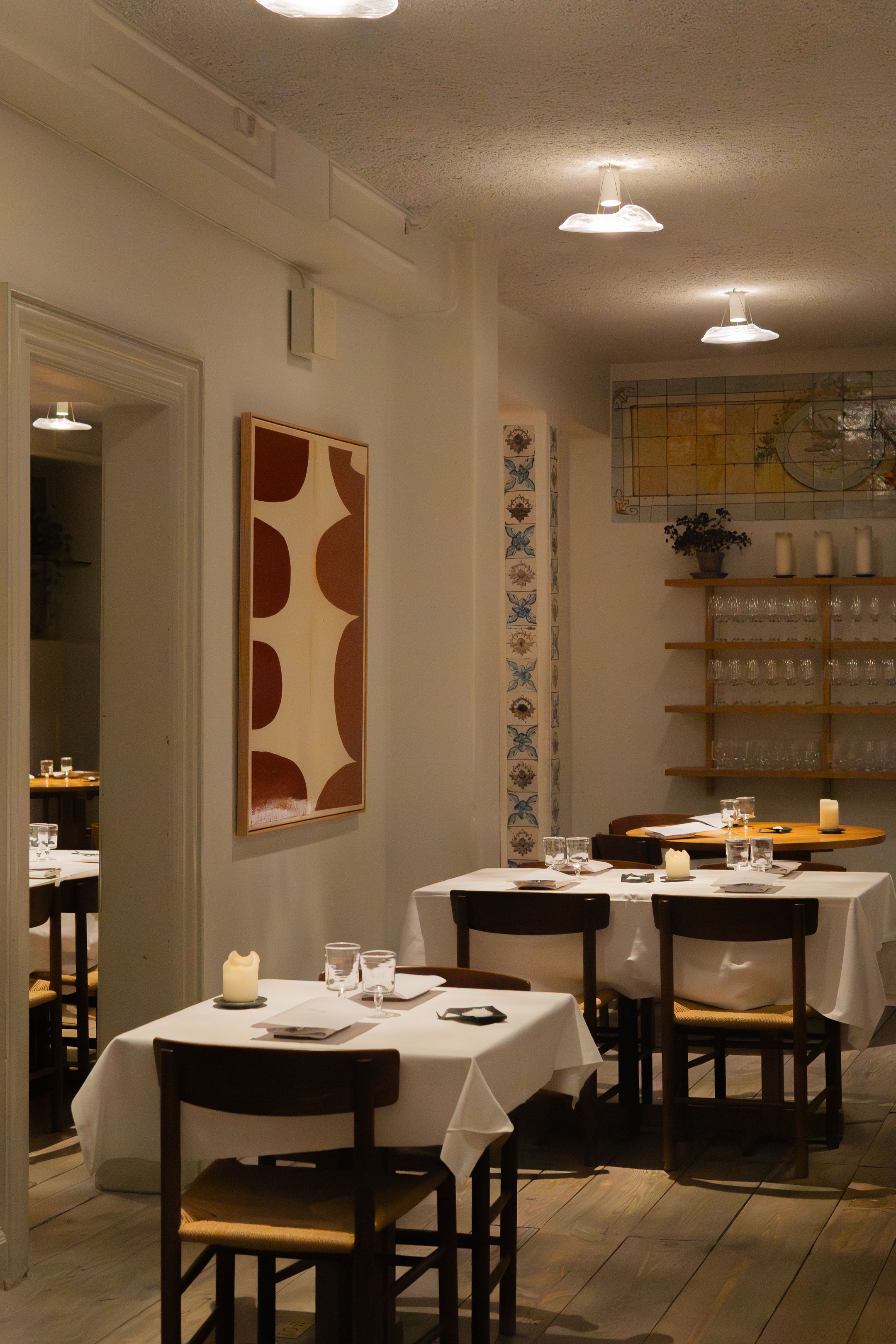 Minimalist restaurant interior with white tablecloths and modern decor on walls.