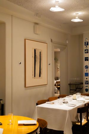 Modern restaurant interior with white tablecloths and bright yellow accent chairs under ceiling lights.