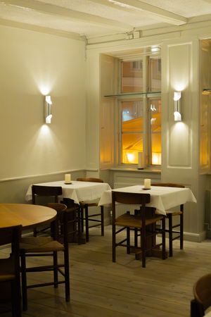 Modern restaurant interior with white tablecloths, wooden floors, and warm wall sconces creating an intimate dining atmosphere.