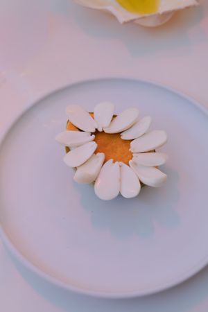 A daisy-shaped cookie or pastry arranged on a plain white plate against a soft pink background.