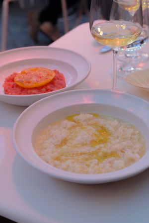 White plates of risotto with olive oil drizzled on top sit on a dining table in warm lighting.