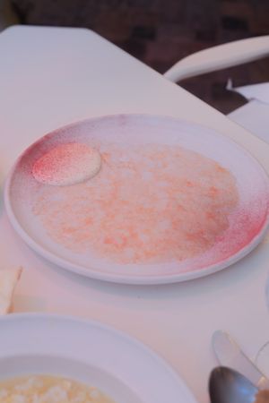 Several plates of pink-tinted risotto are arranged on a dark wooden table under soft lighting.