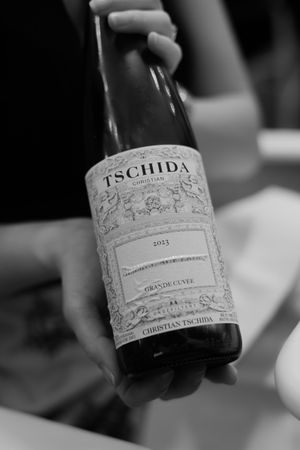 Black and white close-up of a Tschida wine bottle being held, showing its ornate label design.