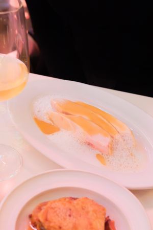 Close-up of elegantly plated salmon dish with foam sauce on white porcelain plate in warm lighting.