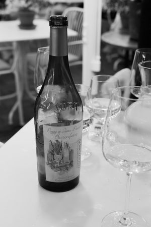 Black and white photo of wine bottles and glasses arranged on a white tablecloth at a formal dining setting.
