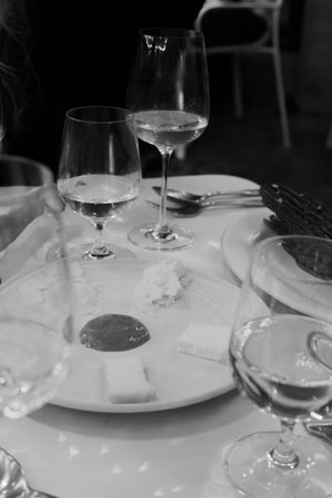 Black and white photo of wine glasses and place settings on a white tablecloth in an upscale restaurant setting.
