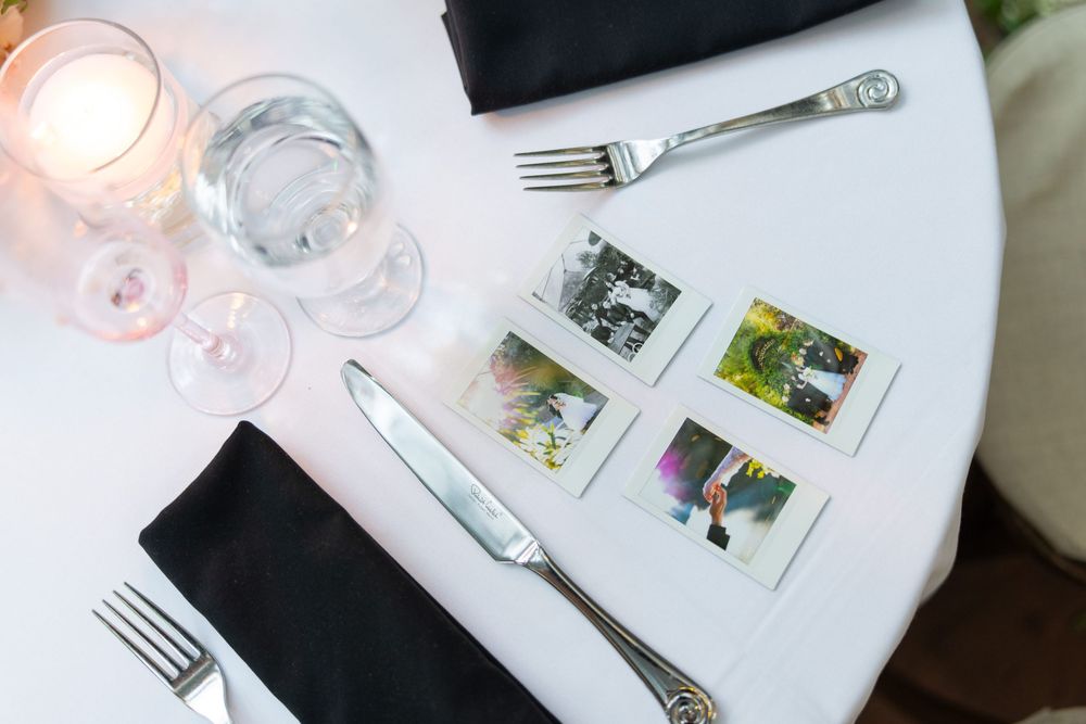 Wedding reception place settings with polaroid photos and wine glasses on white linens.