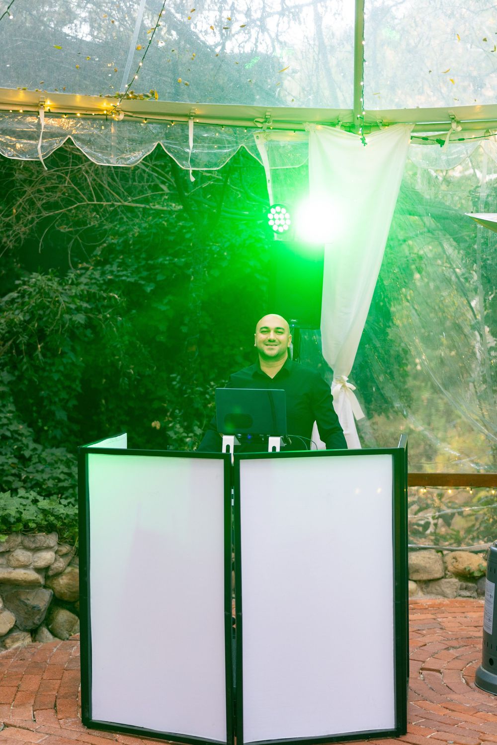 White decorative fabric panels hang from a natural outdoor canopy with green lighting effects creating an ethereal ambiance.