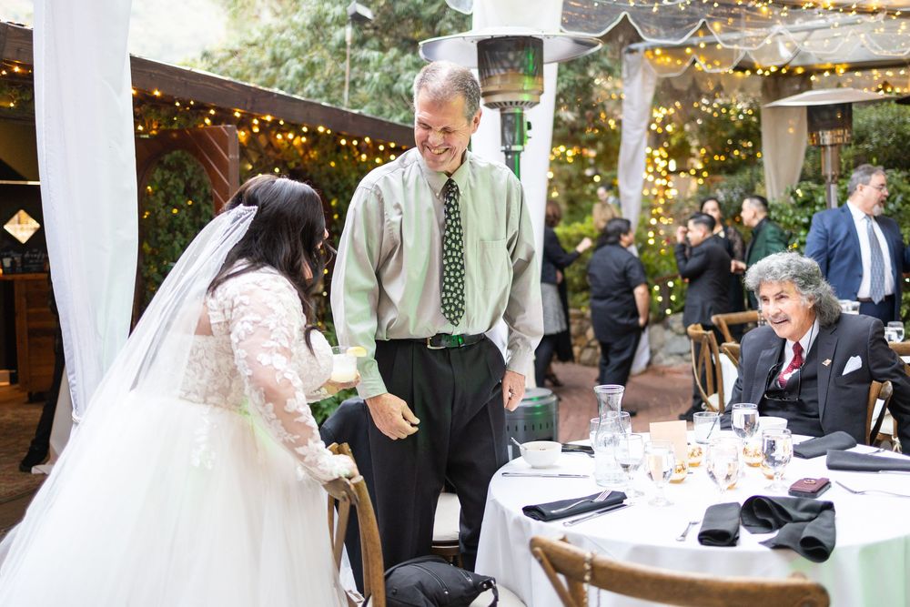 Reception area decorated with string lights and guests gathered at tables for an outdoor wedding celebration.
