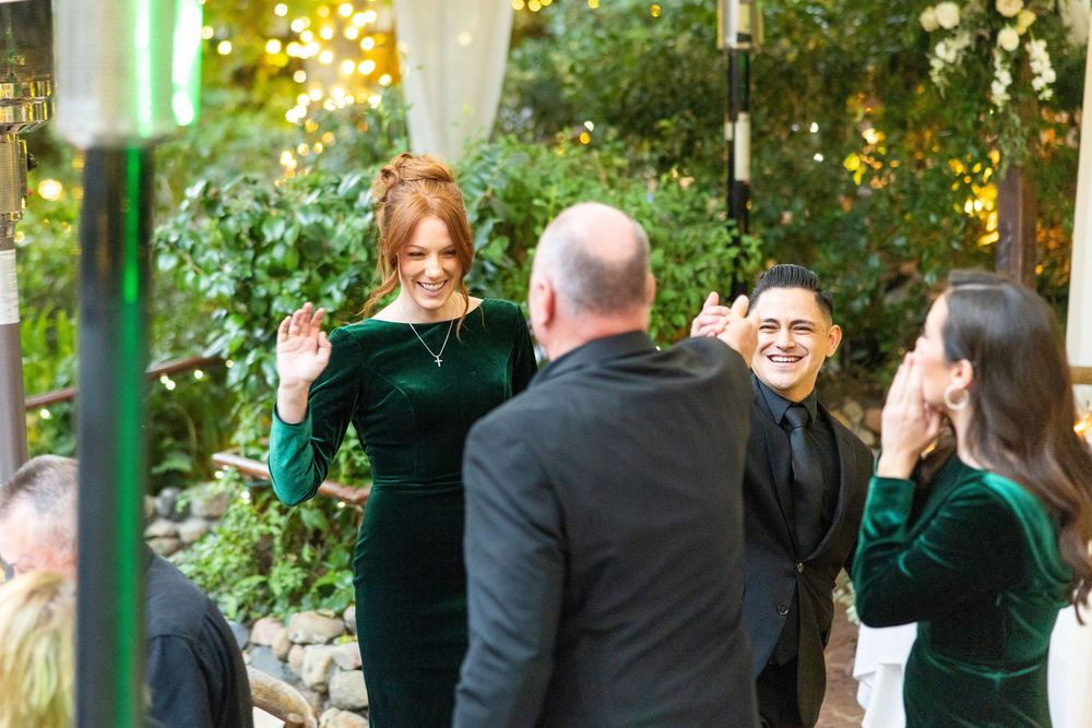 Wedding party gathered outdoors under tented pavilion with golden sunset lighting.