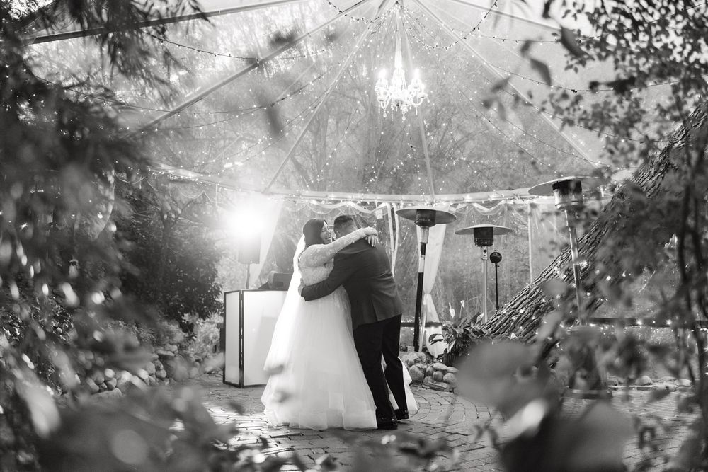 Black and white photograph of guests dancing under an elegant outdoor wedding tent.