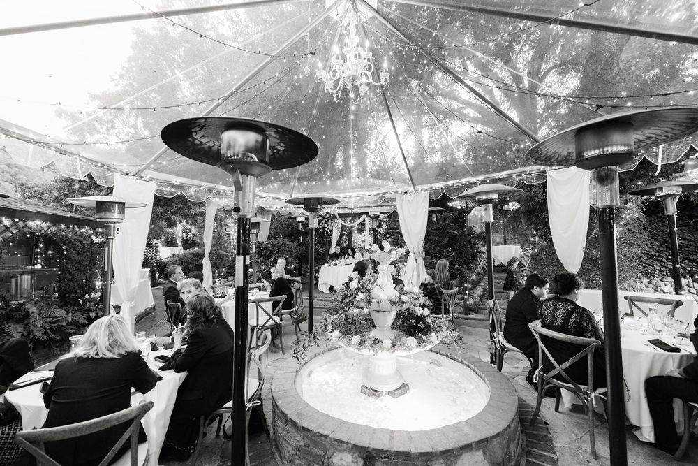 Black and white panoramic view of wedding reception with guests mingling under decorated tent.
