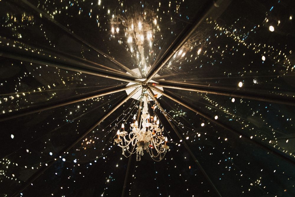 Sparkling chandelier and string lights creating magical ambiance in wedding reception tent.