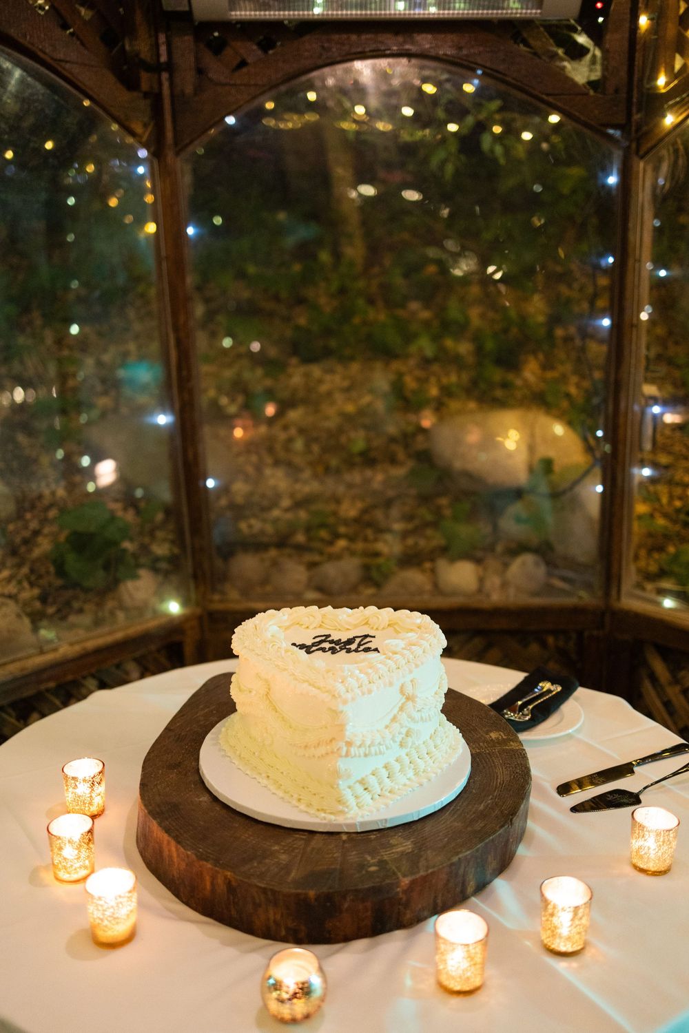 Wedding cake illuminated by candlelight on a rustic wooden cake stand during an evening reception.